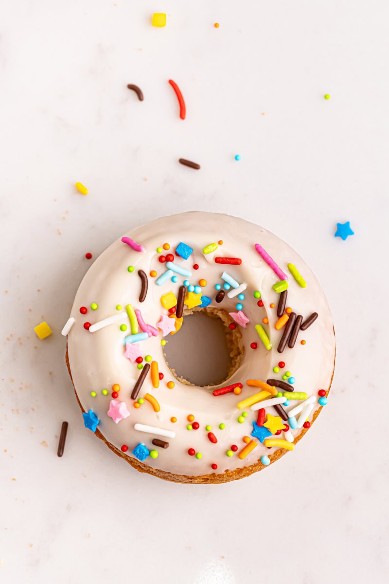 a baked doughnut topped with glaze and sprinkles on a white surface