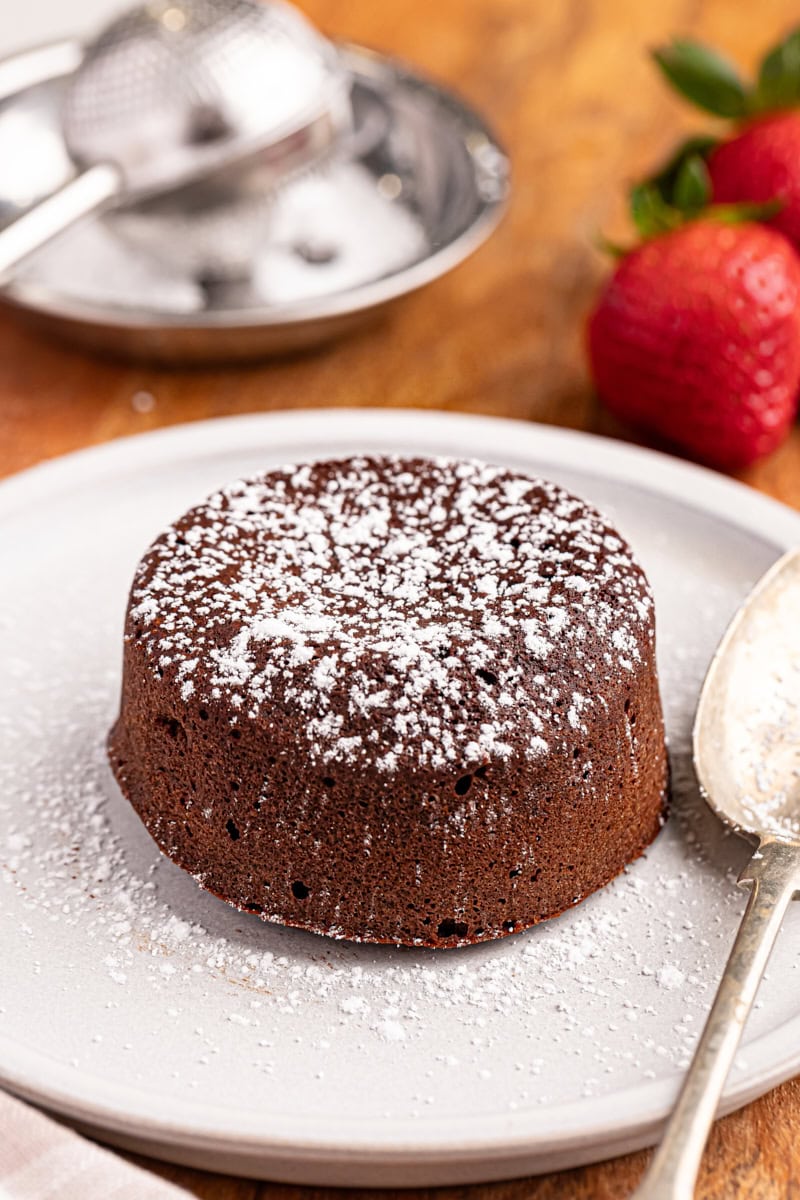 a chocolate lava cake topped with a dusting of confectioners' sugar and served on a white plate