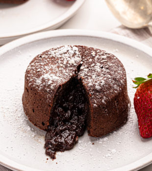 a chocolate lava cake on a white plate with the molten center oozing out of the cake