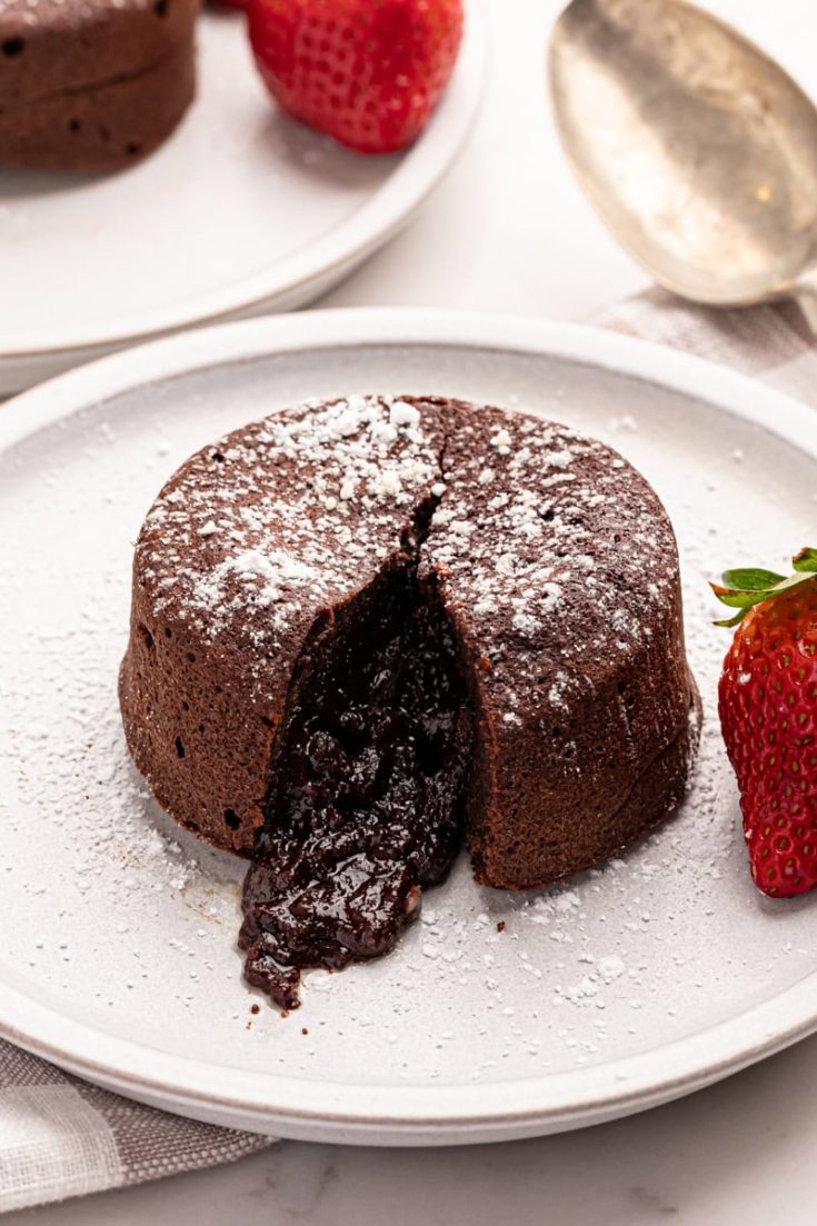 a chocolate lava cake on a white plate with the molten center oozing out of the cake