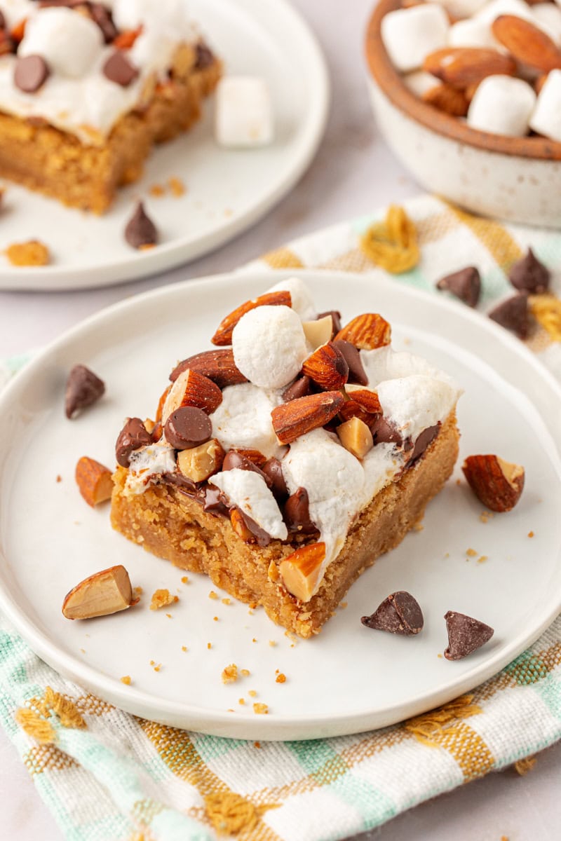 a peanut butter rocky road bar on a white plate with more bars in the background