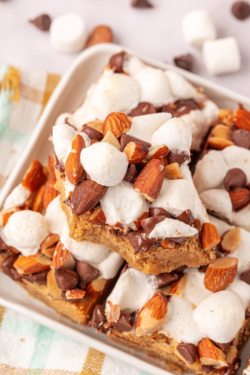 peanut butter rocky road bars stacked on a plate with a bite missing from the top bar