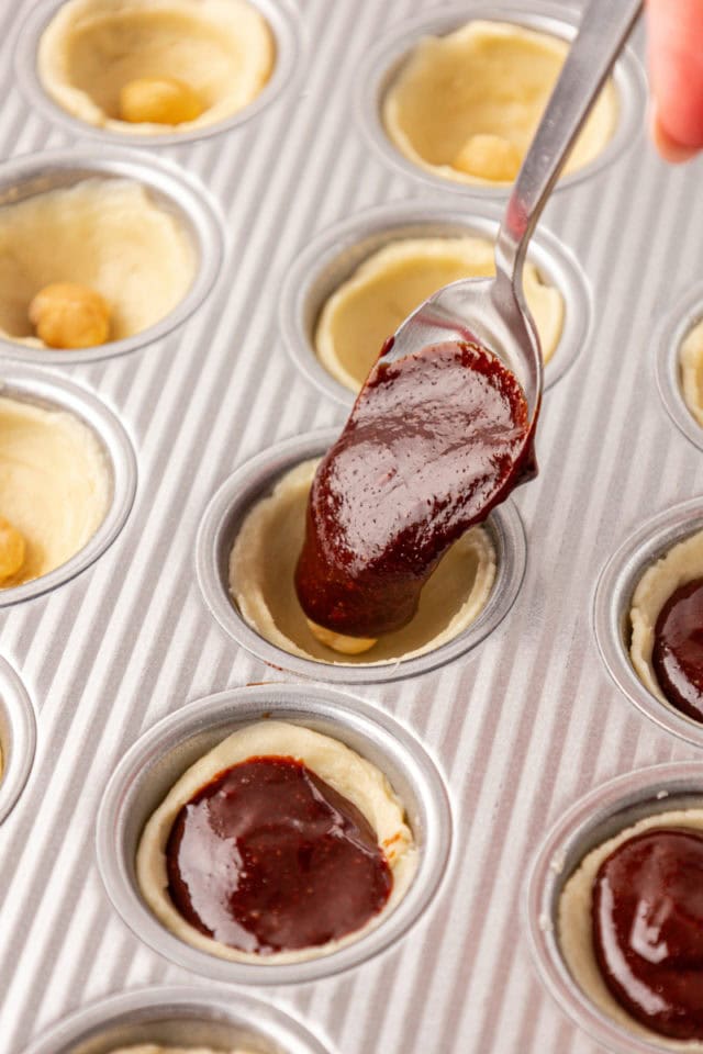 brownie batter being spooned into pie crusts in a mini muffin pan