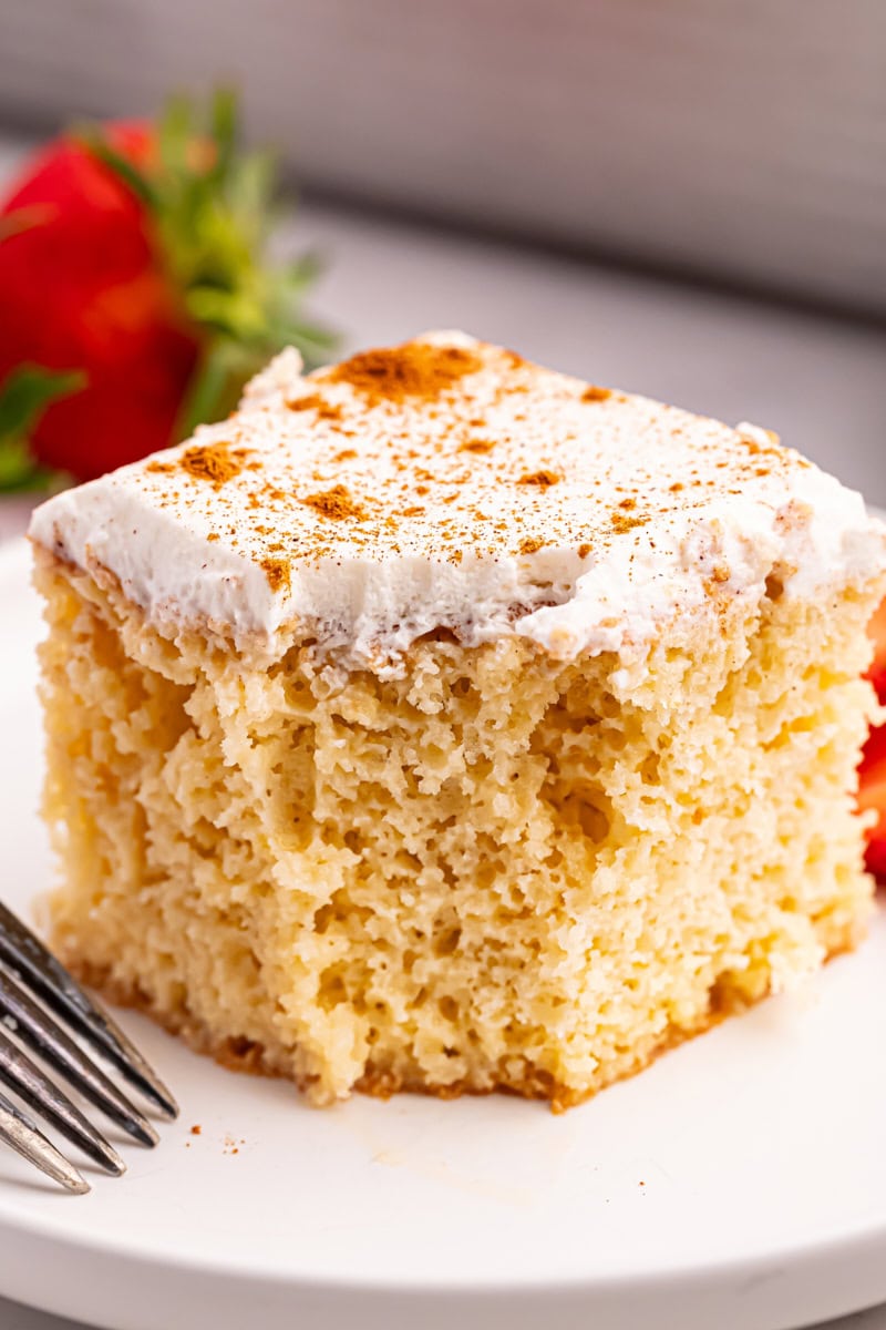 a slice of tres leches cake on a white plate with a bite missing from the cake