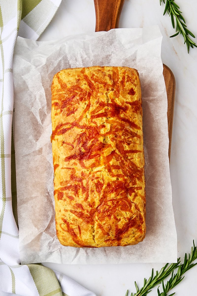 overhead view of herb and cheese quick bread on parchment paper on a wooden cutting board