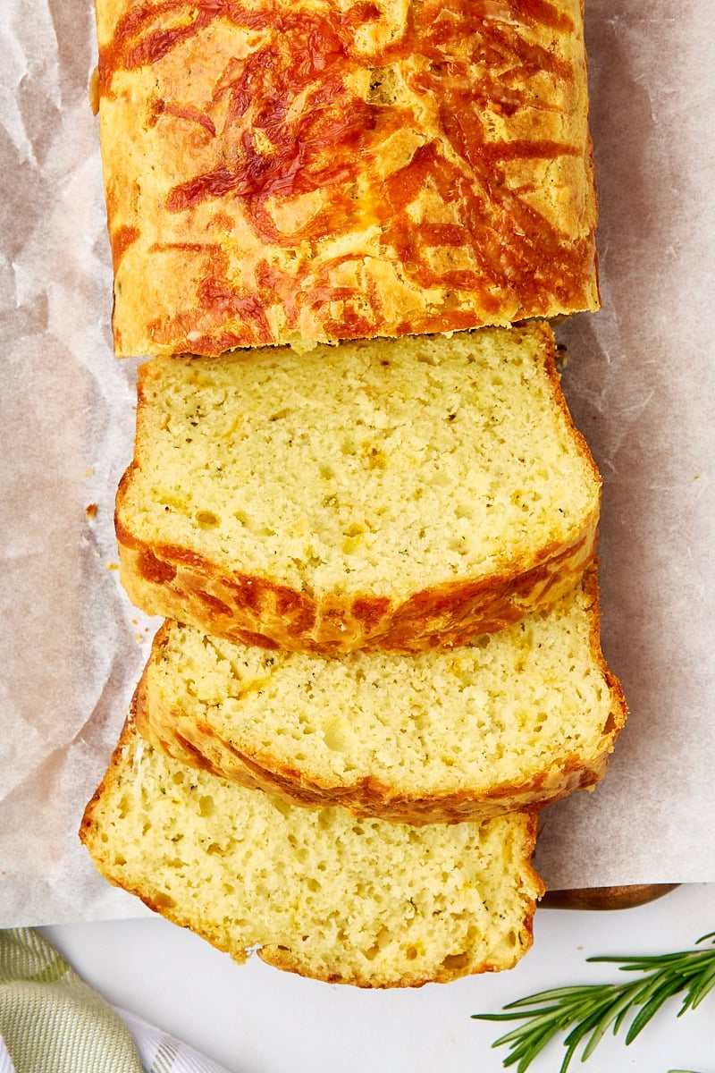 overhead view of partially sliced herb and cheese quick bread on parchment paper