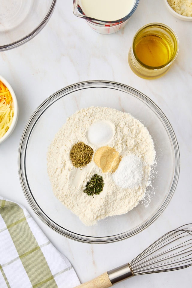 overhead view of flour, baking powder, garlic, and herbs in a mixing bowl