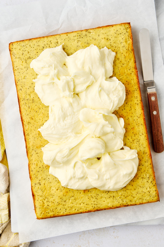 lemon poppy seed cake topped with dollops of frosting just before spreading onto the cake