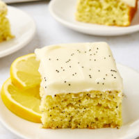 a slice of lemon poppy seed cake on a white plate with more cake in the background