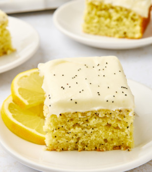 a slice of lemon poppy seed cake on a white plate with more cake in the background