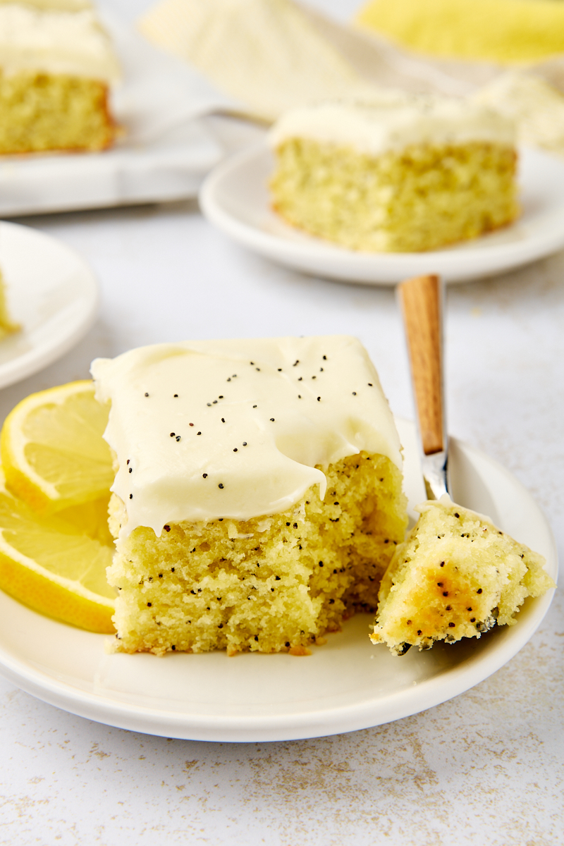 a slice of lemon poppy seed cake on a white plate with a bite on a fork