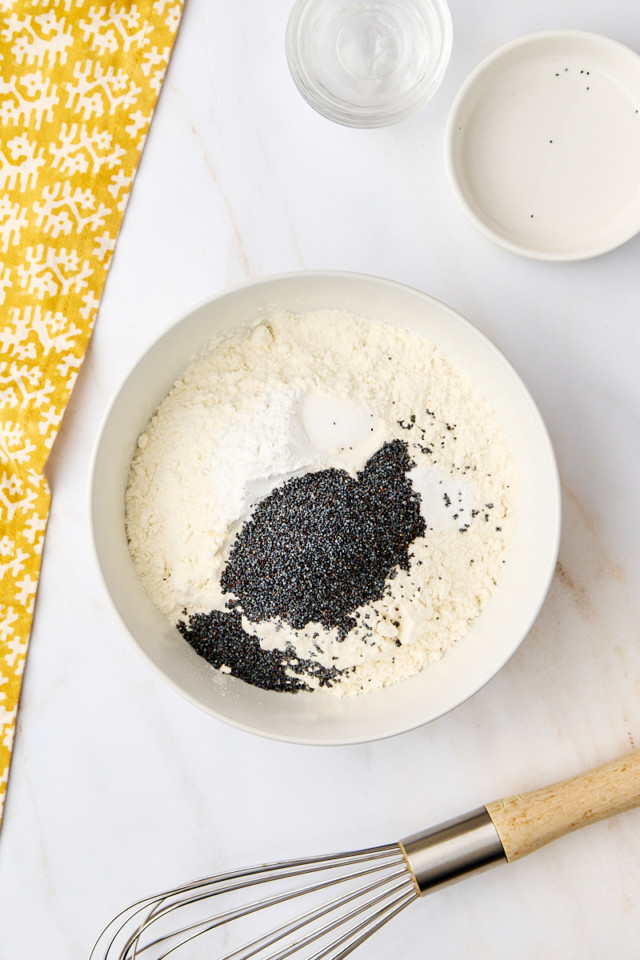 overhead view of flour, baking powder, baking soda, salt, and poppy seeds in a mixing bowl