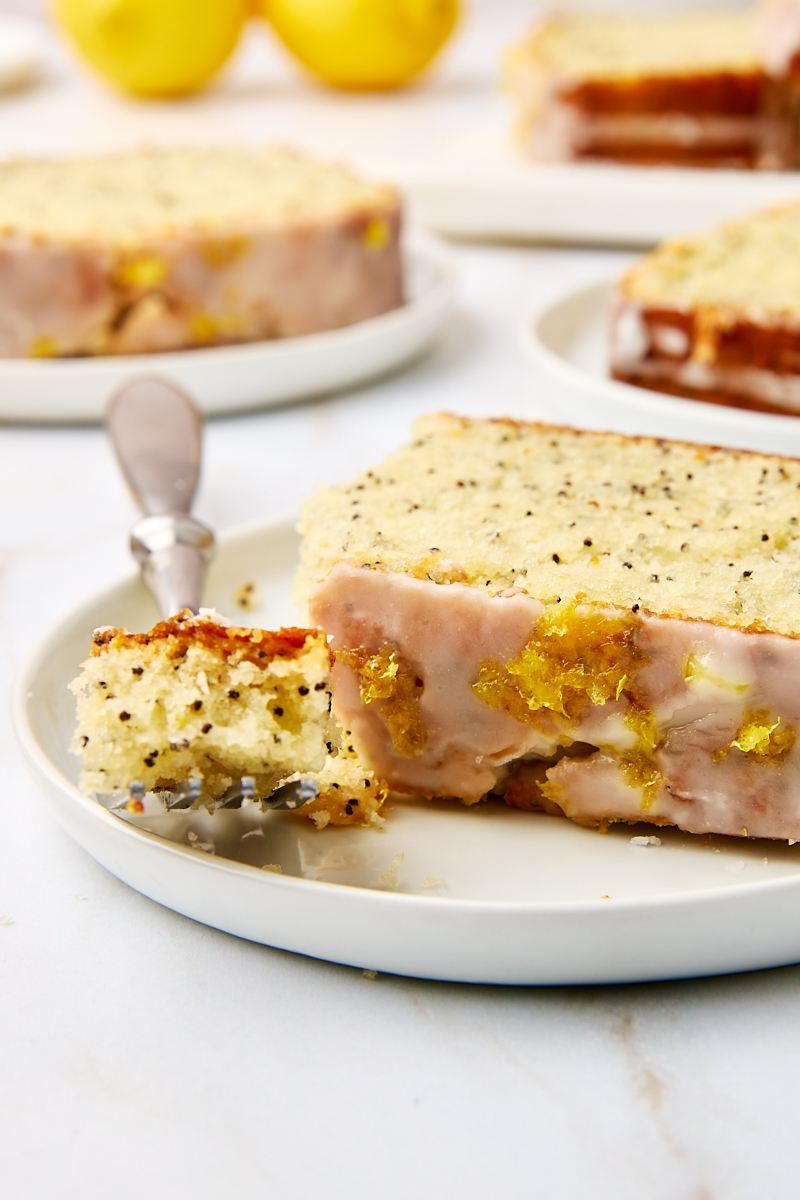 a slice of lemon poppy seed loaf on a white plate with a bite on a fork