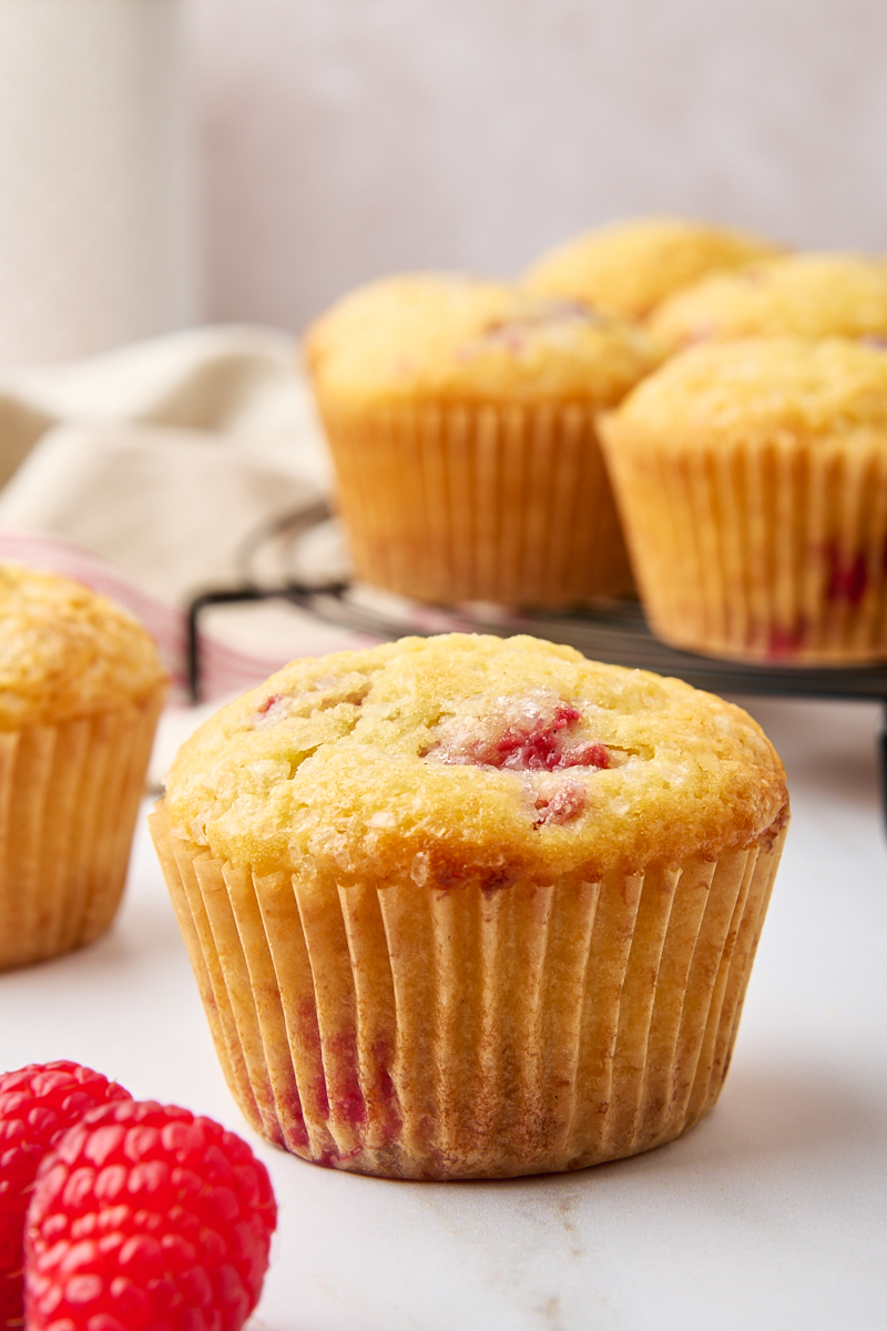 a lemon raspberry muffin on a white countertop with more muffins in the background