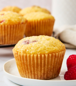 a lemon raspberry muffin on a white plate with more muffins in the background