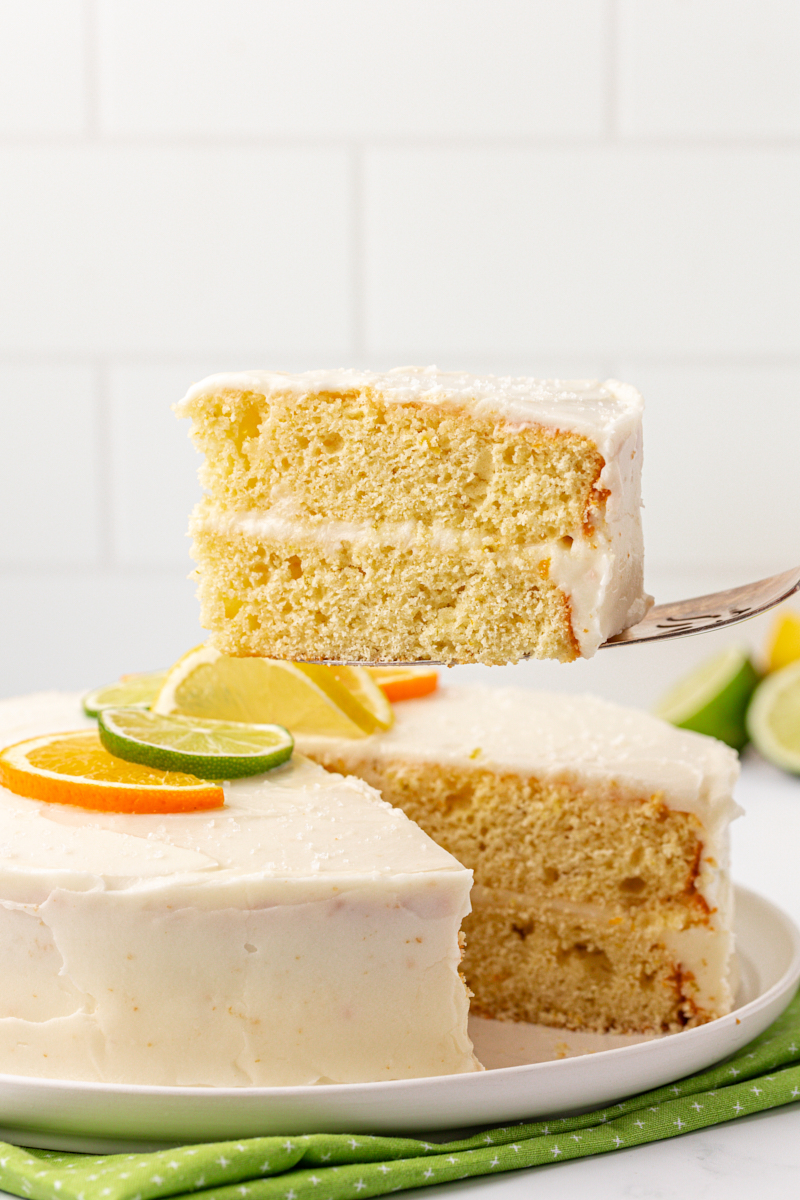 a slice of citrus cake with tequila lime frosting being lifted away from the remaining cake