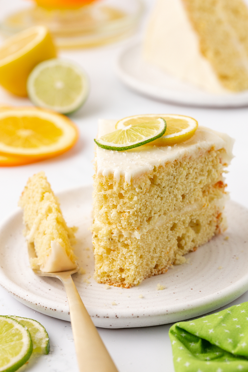 a slice of citrus cake with tequila lime frosting on a plate with a bite on a fork