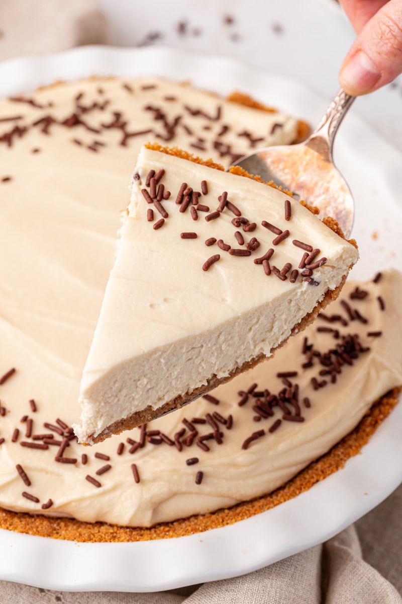 a slice of no-bake Bailey's cheesecake on a pie server with the remaining cheesecake in the background