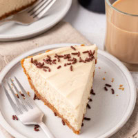 a slice of no-bake Bailey's cheesecake on a white plate with a glass of Bailey's alongside