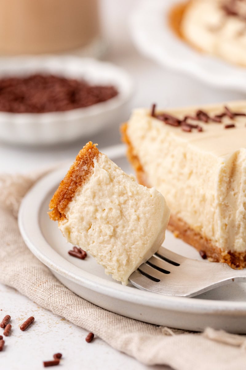 close-up of a bite of no-bake Bailey's cheesecake on a fork on a plate with the remaining slice of cheesecake