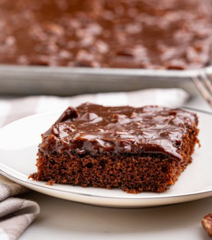 a slice of Texas sheet cake on a white plate with the remaining cake in the background