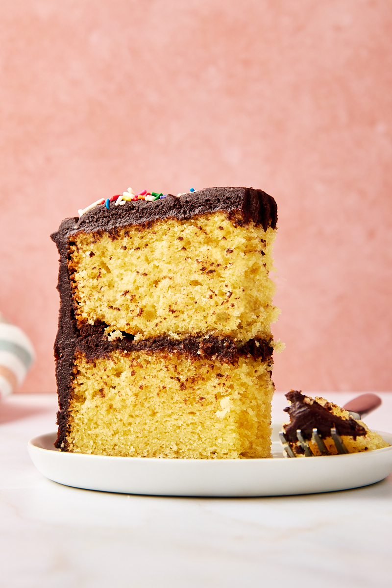 a slice of yellow cake with chocolate frosting on a white plate with a bite on a fork