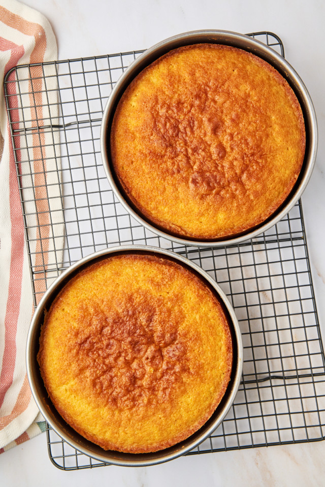 overhead view of freshly baked yellow cake layers in cake pans on a wire rack