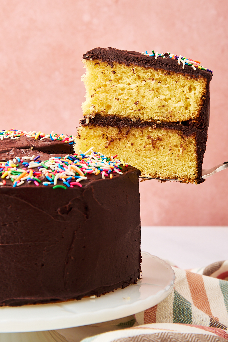 a slice of yellow cake with chocolate frosting being lifted from the remaining cake