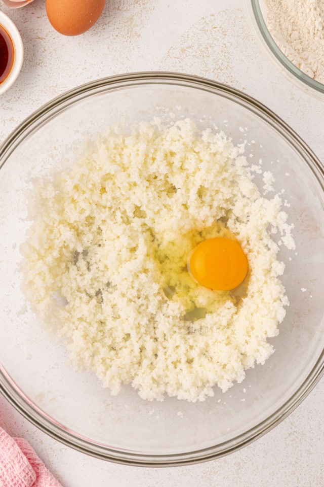 overhead view of egg added to creamed butter and sugar in a glass mixing bowl