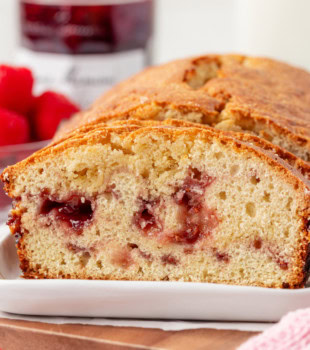 partially sliced berry swirl pound cake on a white plate with fresh raspberries and a jar of raspberry preserves in the background
