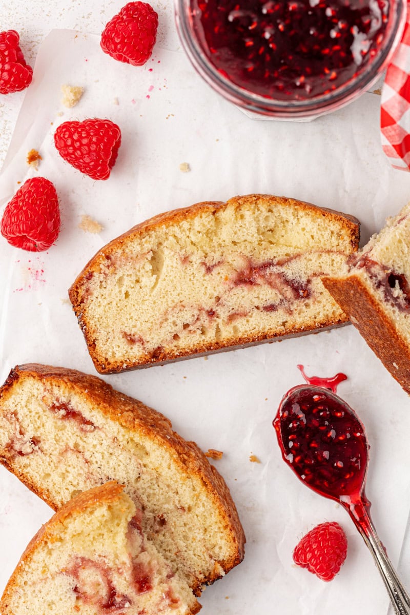a few slices of berry swirl pound cake on parchment paper along with fresh raspberries and a spoonful of raspberry preserves