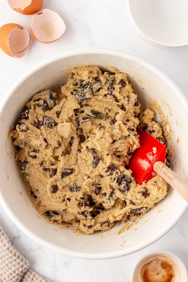 overhead view of mixed Oreo chocolate chip cookie dough in a white mixing bowl with a red spatula resting in the dough