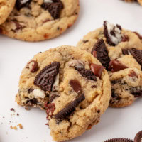 an Oreo chocolate chip cookie with a bite missing, partially propped on top of another cookie; more cookies surrounding