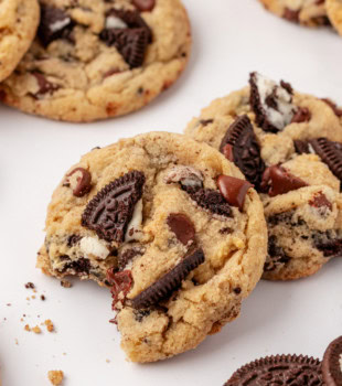 an Oreo chocolate chip cookie with a bite missing, partially propped on top of another cookie; more cookies surrounding