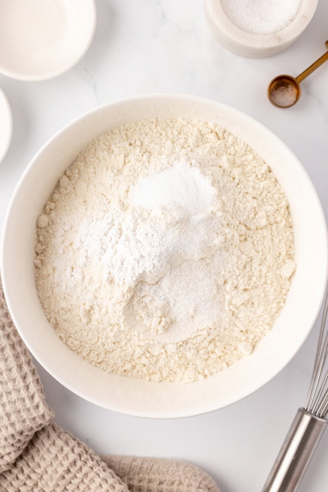 overhead view of flour, baking powder, baking soda, and salt in a white mixing bowl