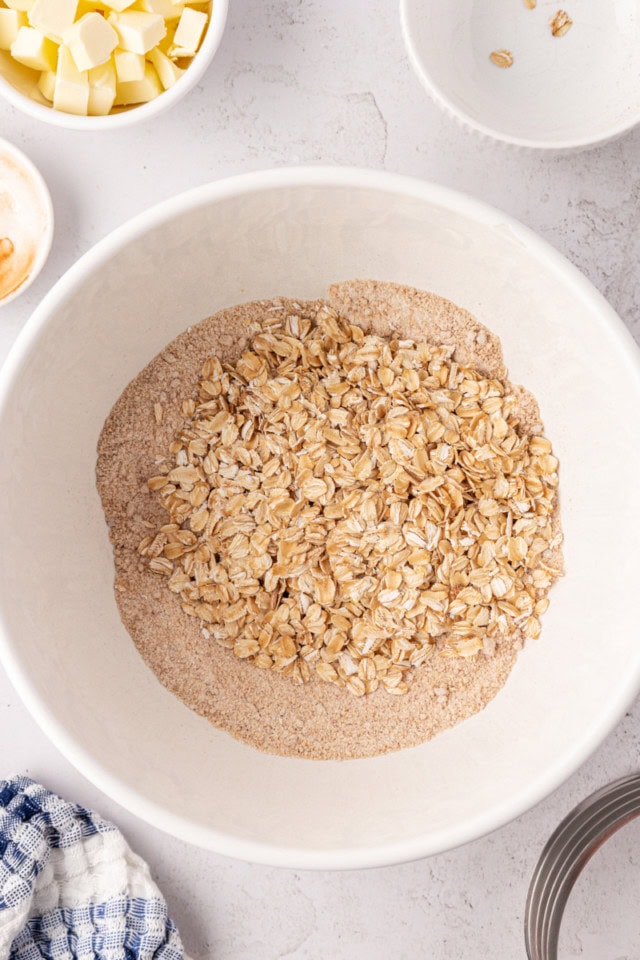 overhead view of oats added to a mixture of flour, brown sugar, cinnamon, and salt in a white mixing bowl