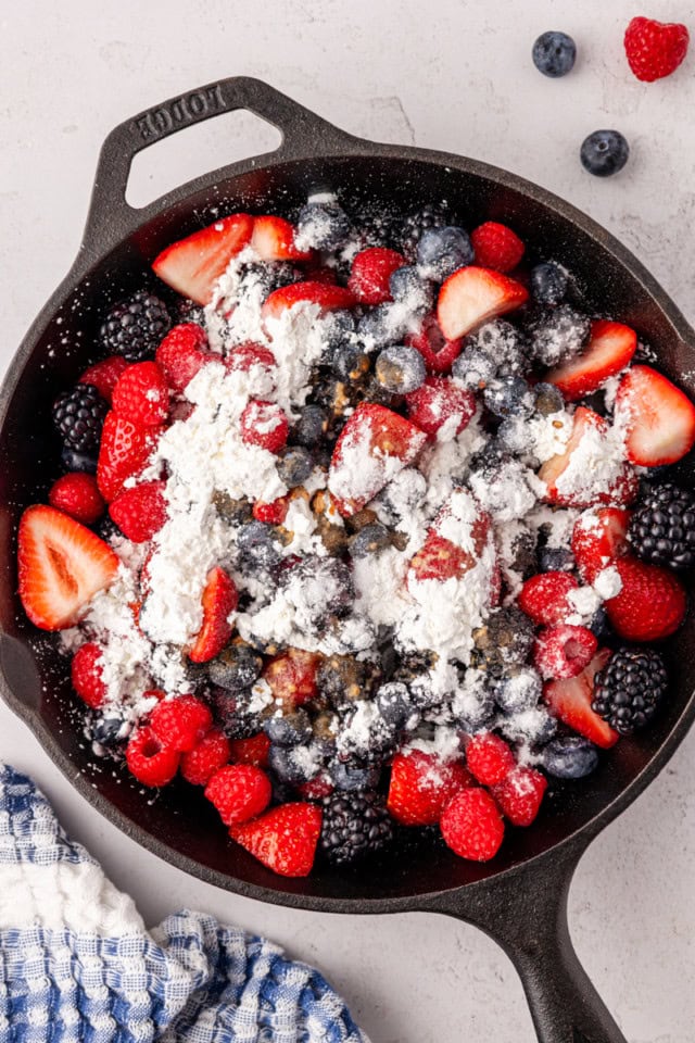 overhead view of mixed berries, sugar, cornstarch, and vanilla extract in a cast-iron skillet