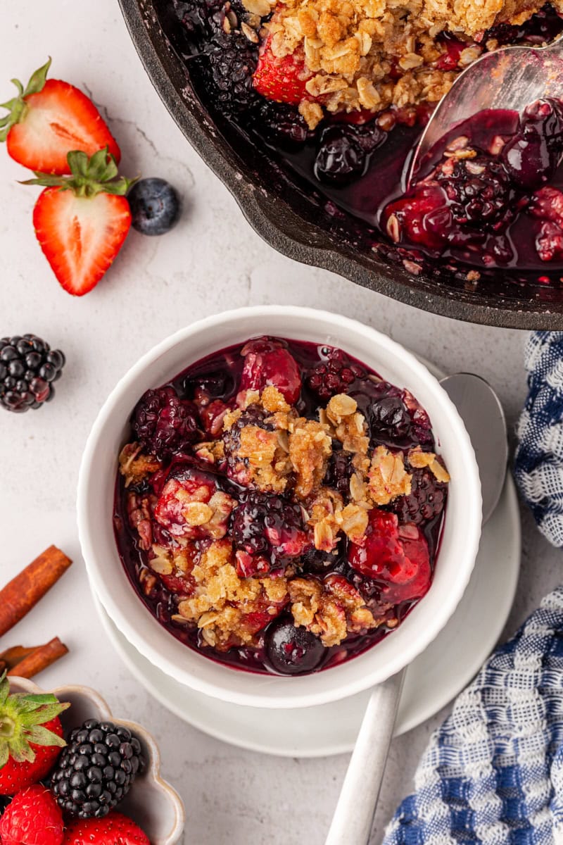 overhead view of berry crisp in a white bowl with the remaining crisp in a skillet partially visible