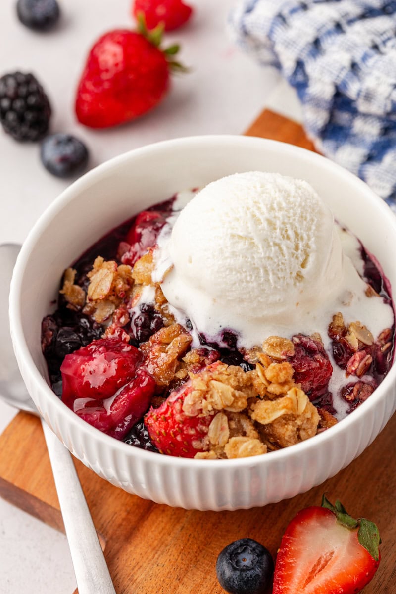 berry crisp served in a white bowl with a scoop of vanilla ice cream