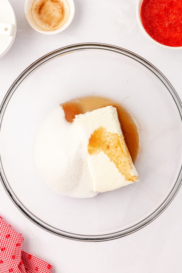 overhead view of cream cheese, sugar, and vanilla extract in a glass mixing bowl