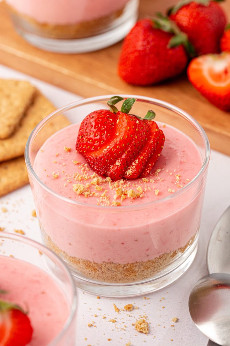 a strawberry no-bake cheesecake topped with strawberry slices and graham cracker crumbs; another cheesecake and fresh strawberries partially visible in the background