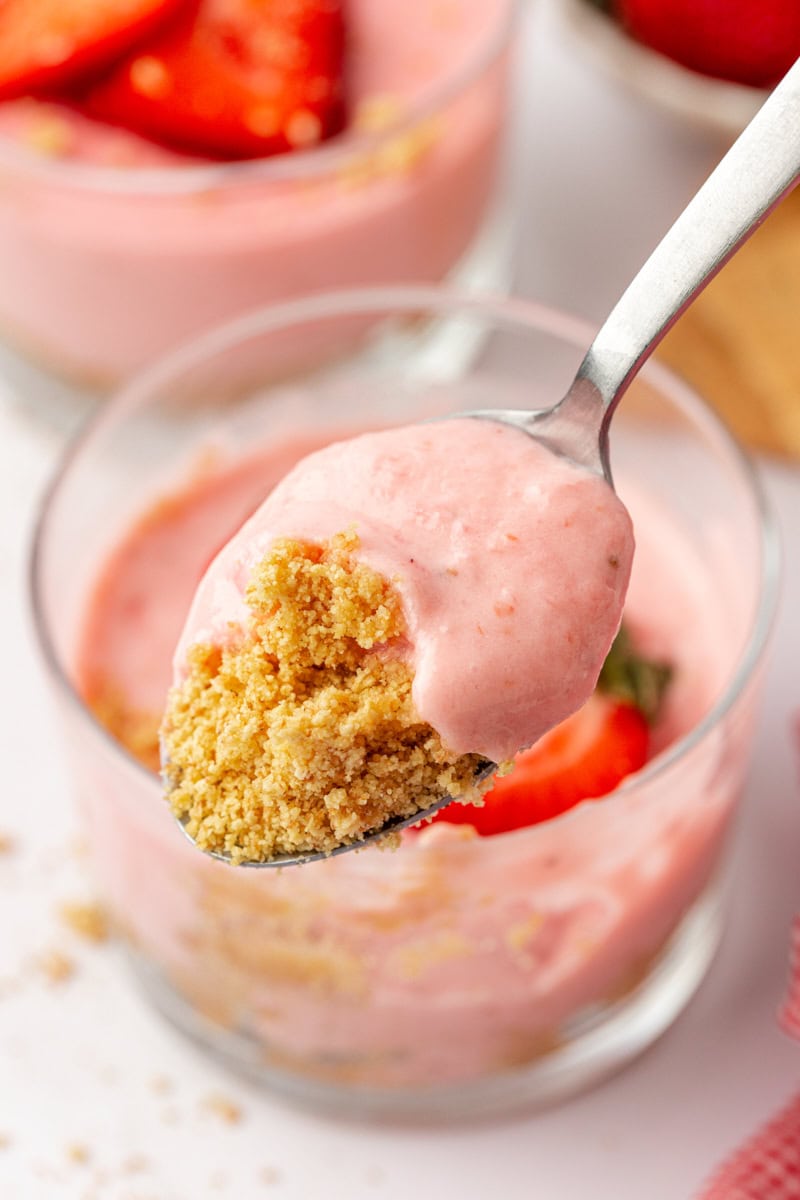 a bite of strawberry no-bake cheesecake on a spoon with the remaining cheesecake in the background