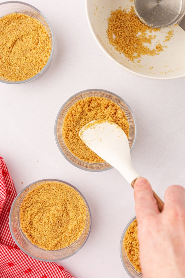 overhead view of graham cracker crust being pressed into the bottom of a small glass