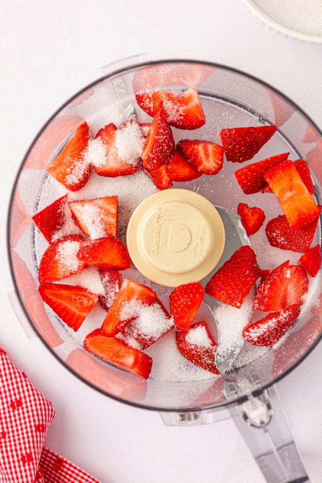 overhead view of strawberries and sugar in the bowl of a food processor