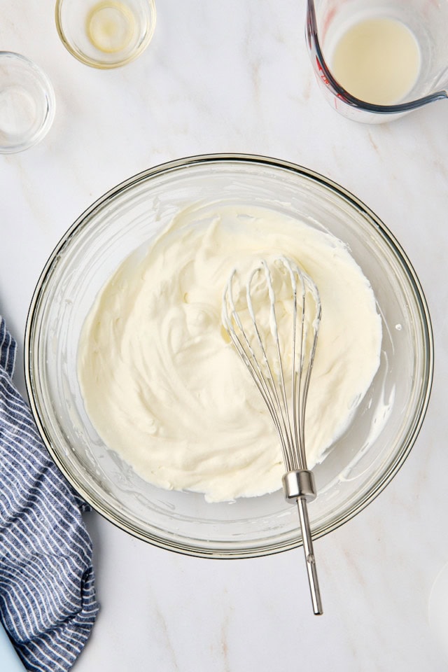 overhead view of whipped cream in a glass mixing bowl with a whisk resting in the cream