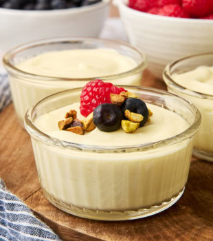 white chocolate mousse in a clear ramekin on a wooden board, surrounded by more servings of mousse and bowls of fresh berries