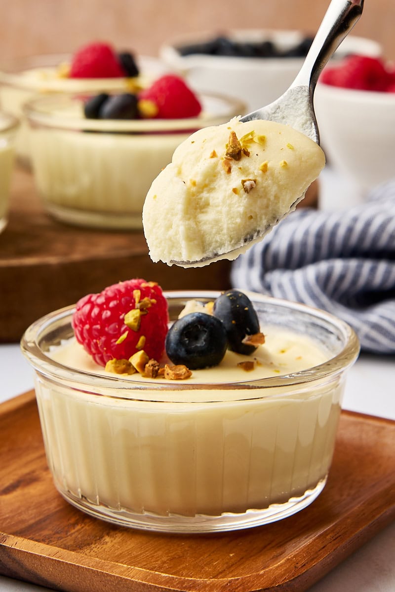 a spoonful of white chocolate mousse over the remaining mousse in a clear ramekin; more mousse and bowls of fresh berries in the background