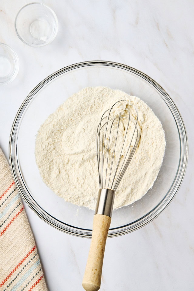 overhead view of combined dry ingredients for yogurt cake in a glass mixing bowl with a whisk resting inside the bowl