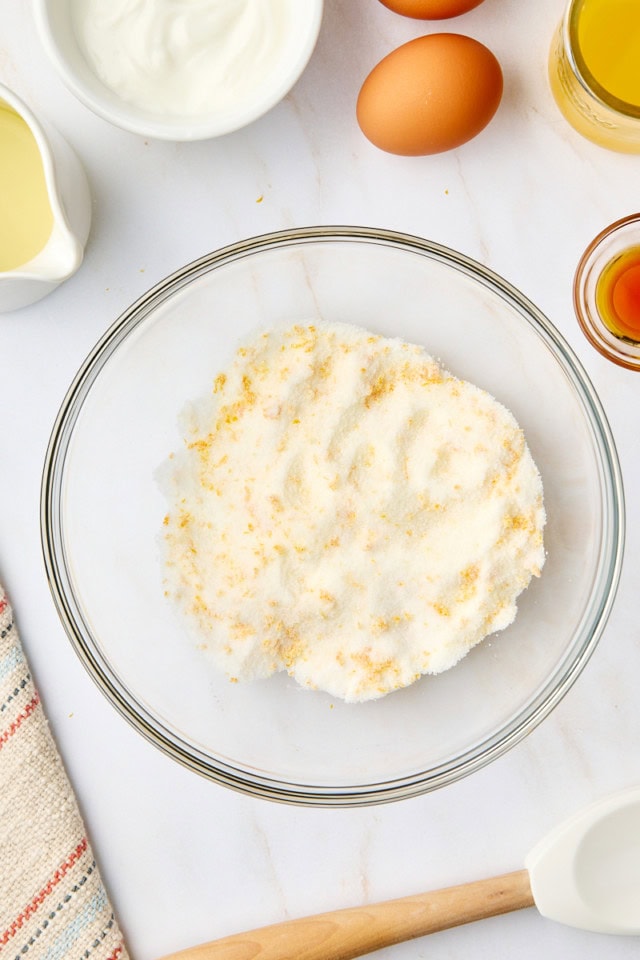 overhead view of orange zest mixed with granulated sugar in a glass mixing bowl