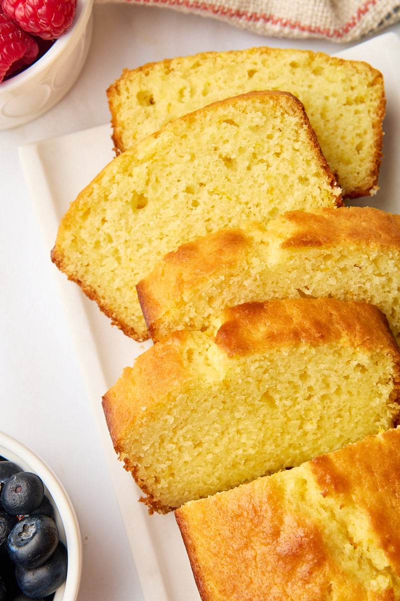 four slices of yogurt cake fanned out next to the remaining cake and bowls of fresh berries